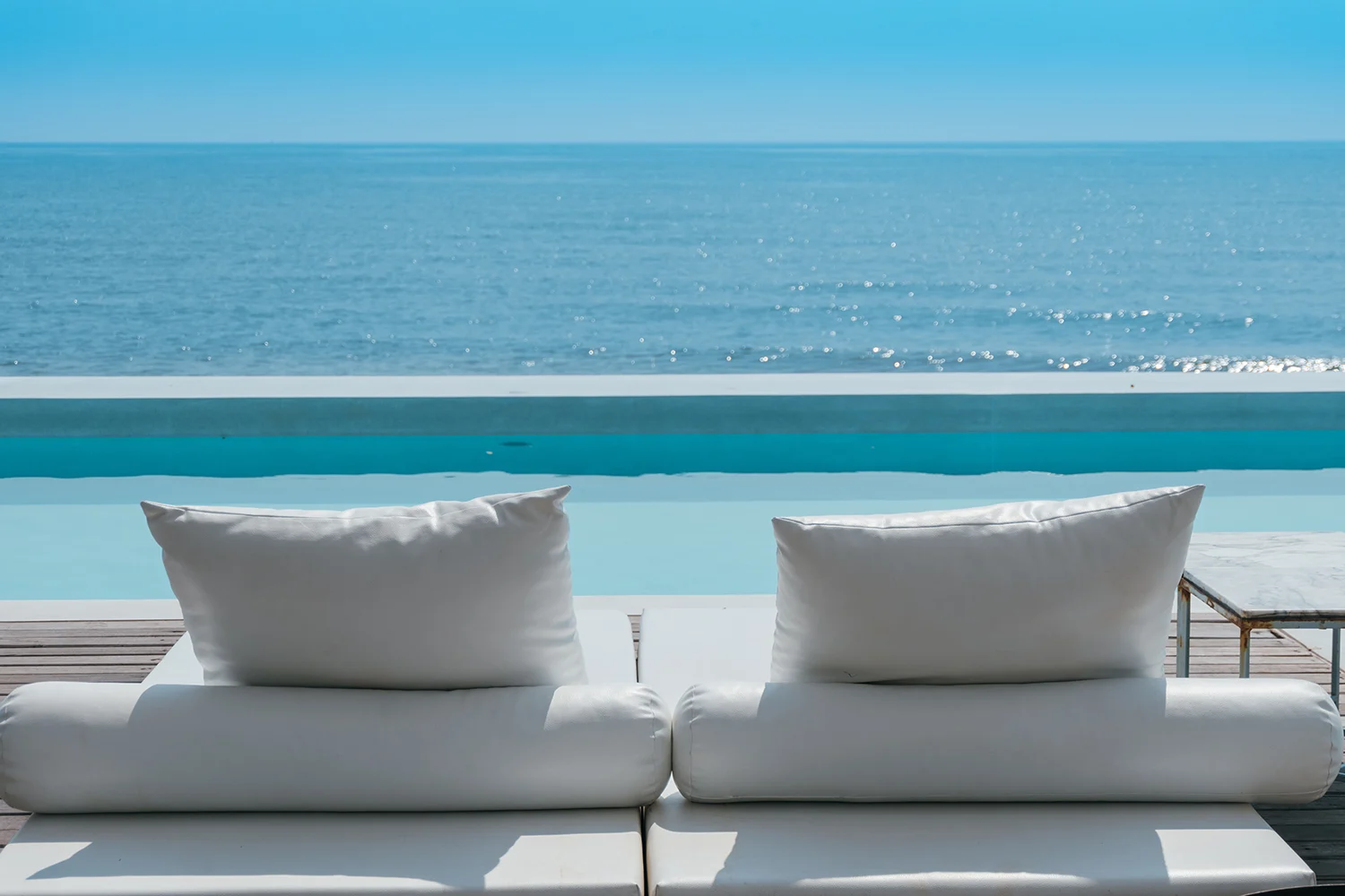 White poolside sofa looking out over an infinity pool to the sea